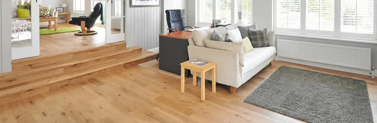 A modern living room with professionally installed laminate flooring, a beige sofa, a small side table, a gray rug, and large windows with white shutters in Arlington, TX